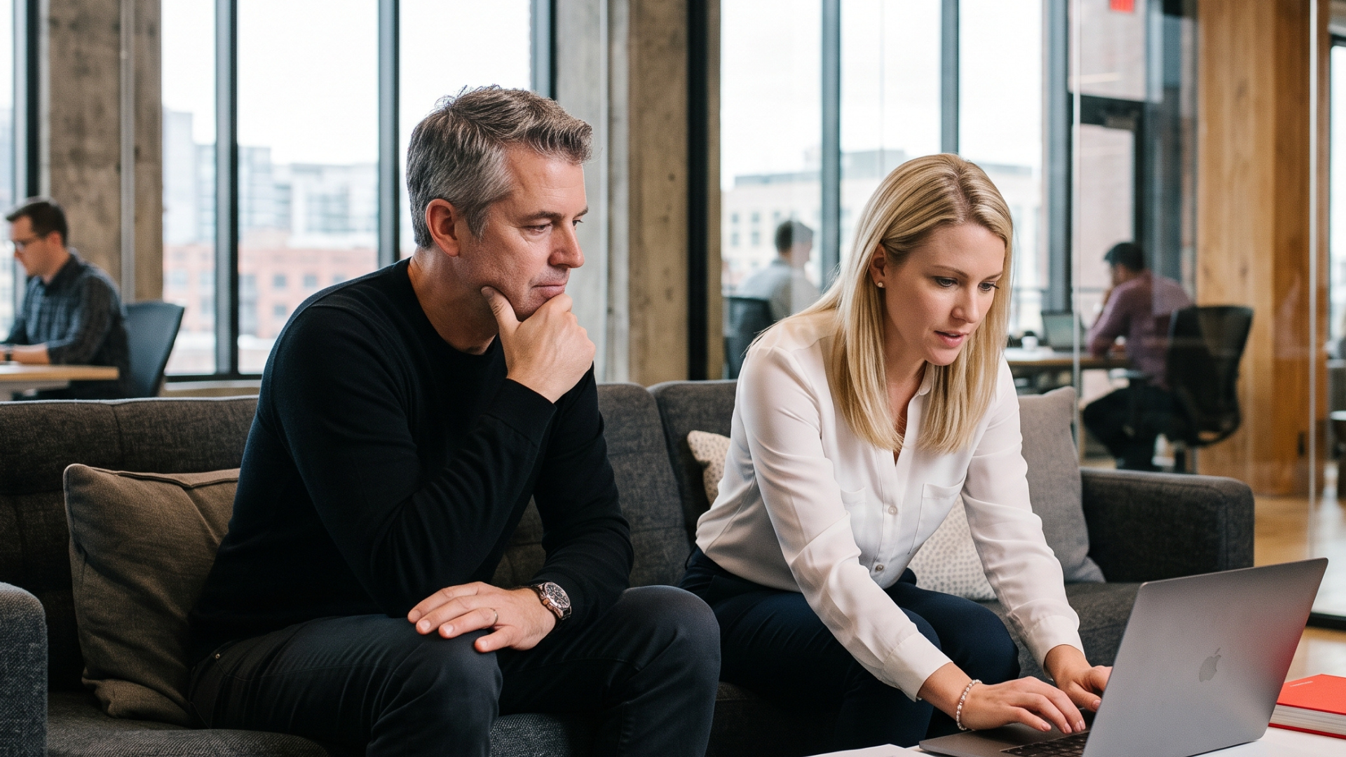 Two colleagues reviewing a course storyboard together on a laptop in a bright open-plan office