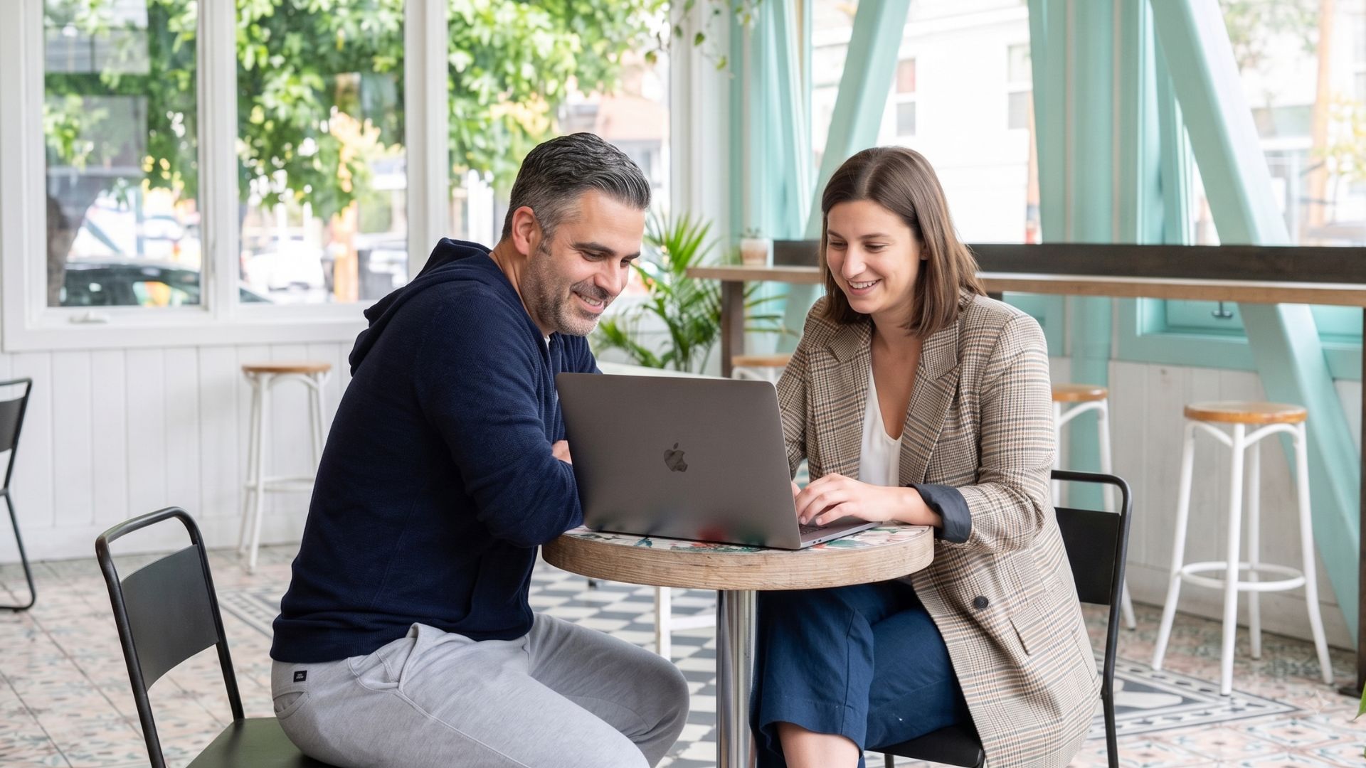 Two colleagues reviewing training content together on a laptop in a bright cafe workspace